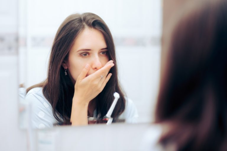 Woman Holding Toothbrush Having a Toothache Looking in the Mirror
