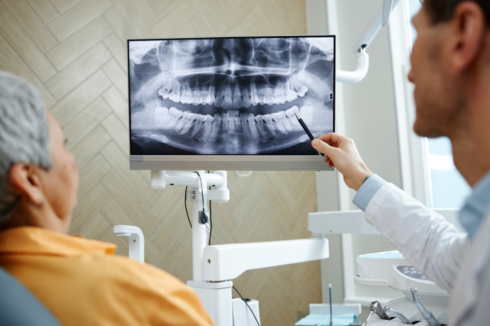 Back view close-up of male dentist pointing at teeth X-ray image on screen during consultation