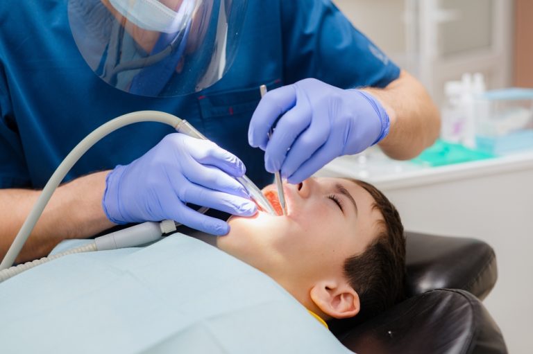 Cute little boy is sitting in a dental chair with a scared expression on his face, afraid to treat his teeth