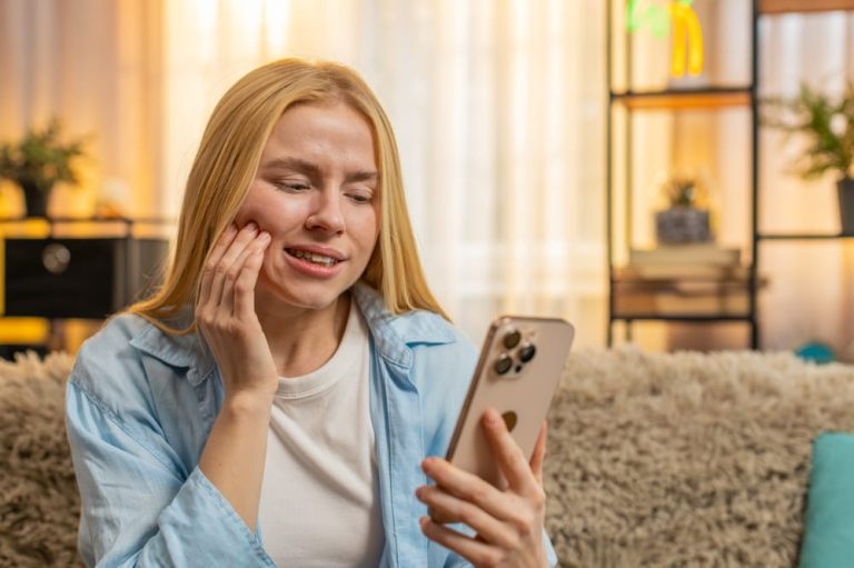 Young woman holding cheek at home, showing tension and urgent need for dental care.