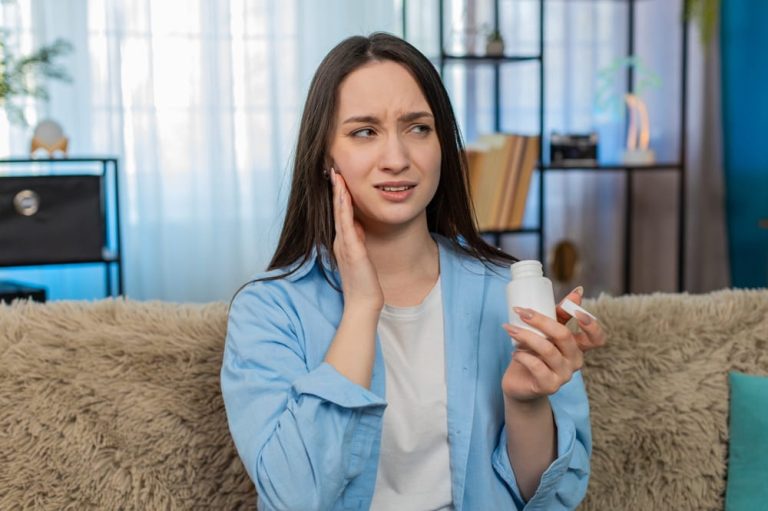 Young ill woman at home suffering from severe toothache, holding cheek painfully, tiredly searching for painkiller pills
