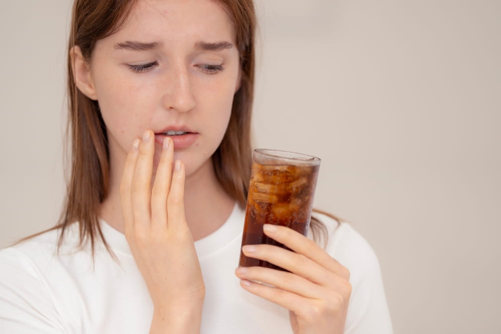 Young woman with toothache holding a glass of cold soda