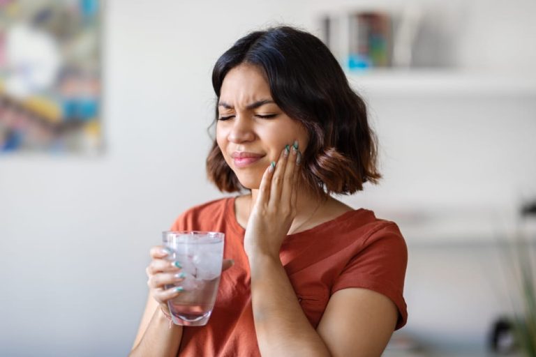 Sensitive Teeth. Young arab woman drinking water with ice and touching her cheek