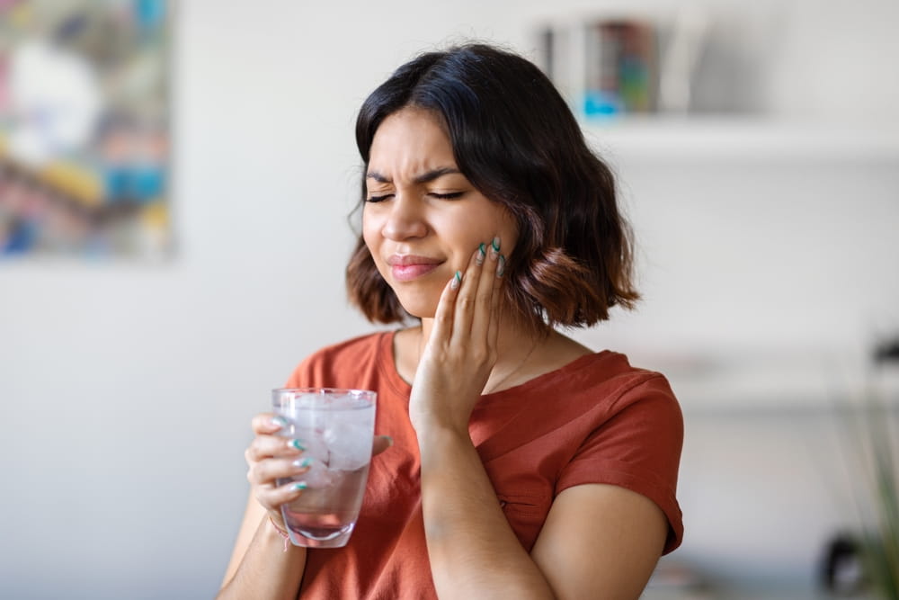 Sensitive Teeth. Young arab woman drinking water with ice and touching her cheek
