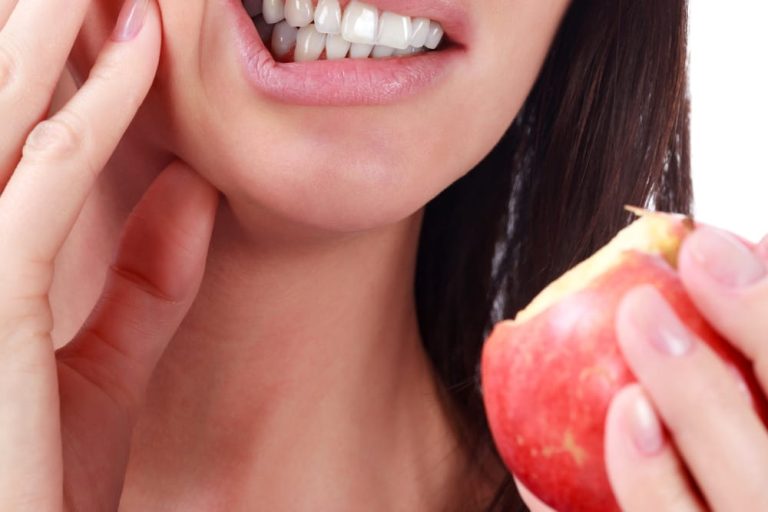 Tooth sensitivity. Young woman with sensitive teeth and eat a apple