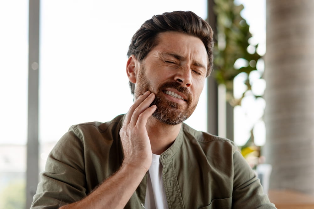 Bearded man experiencing intense toothache, pressing his hand against his cheek in a moment of discomfort and pain