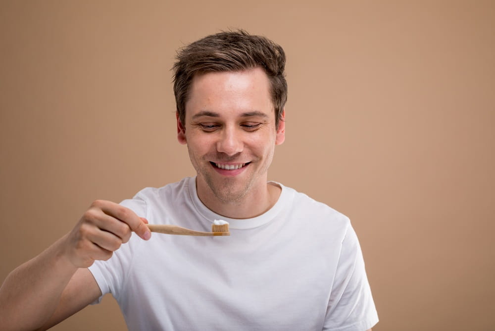 A smiling man in a white t-shirt holds a toothbrush with toothpaste